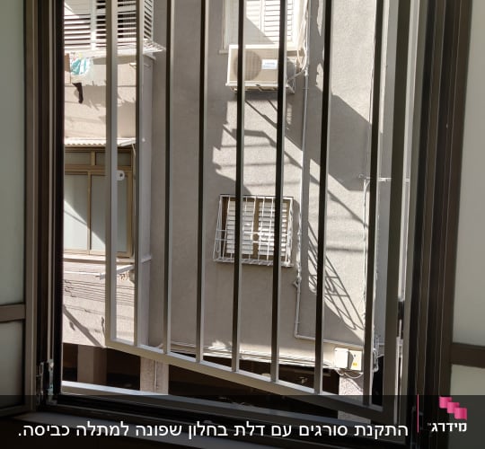 חלון פתוח עם סורגי מתכת מול בניין סמוך